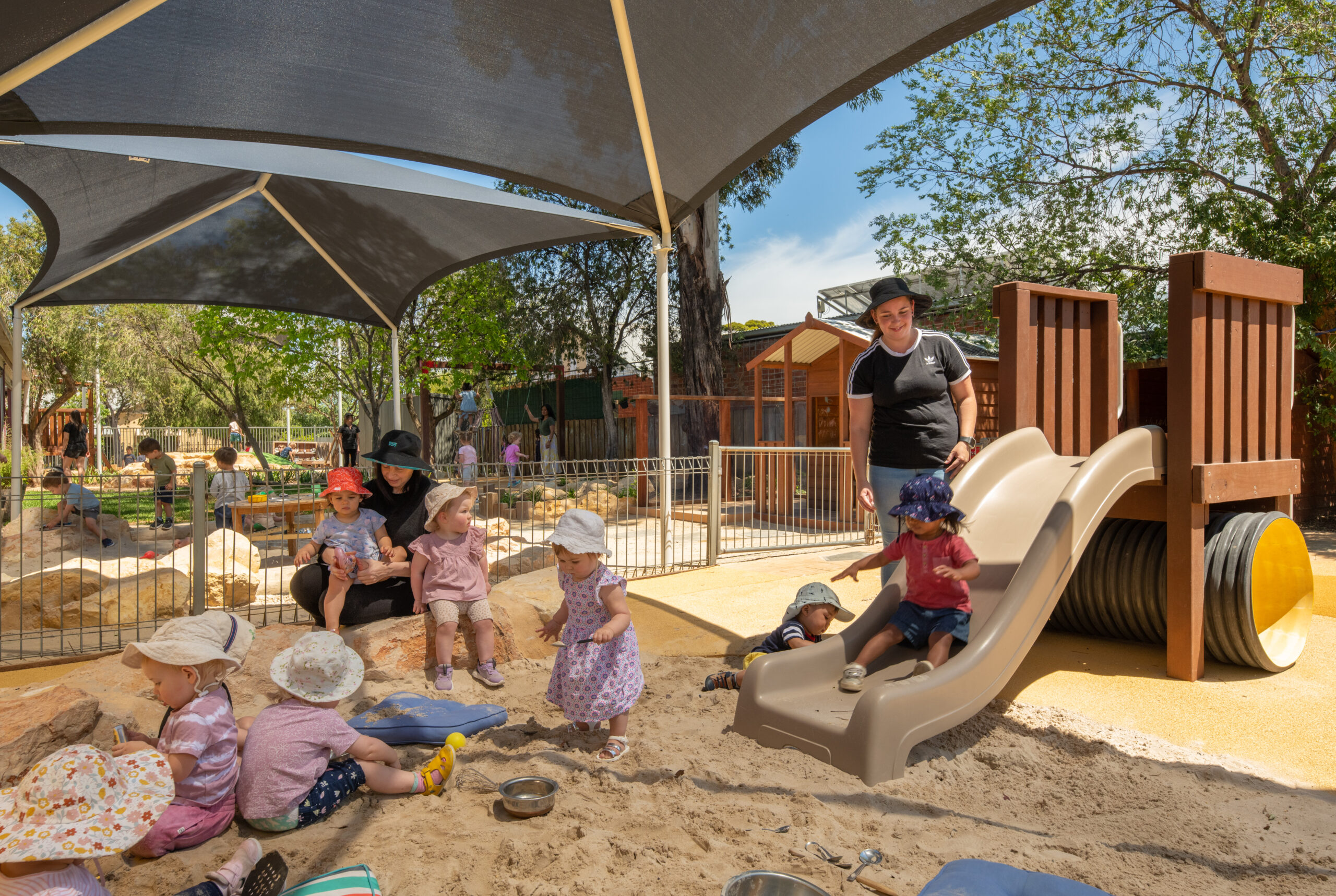 Educators and babies playing with the slide and sandpit at St Morris Community Child Care Centre