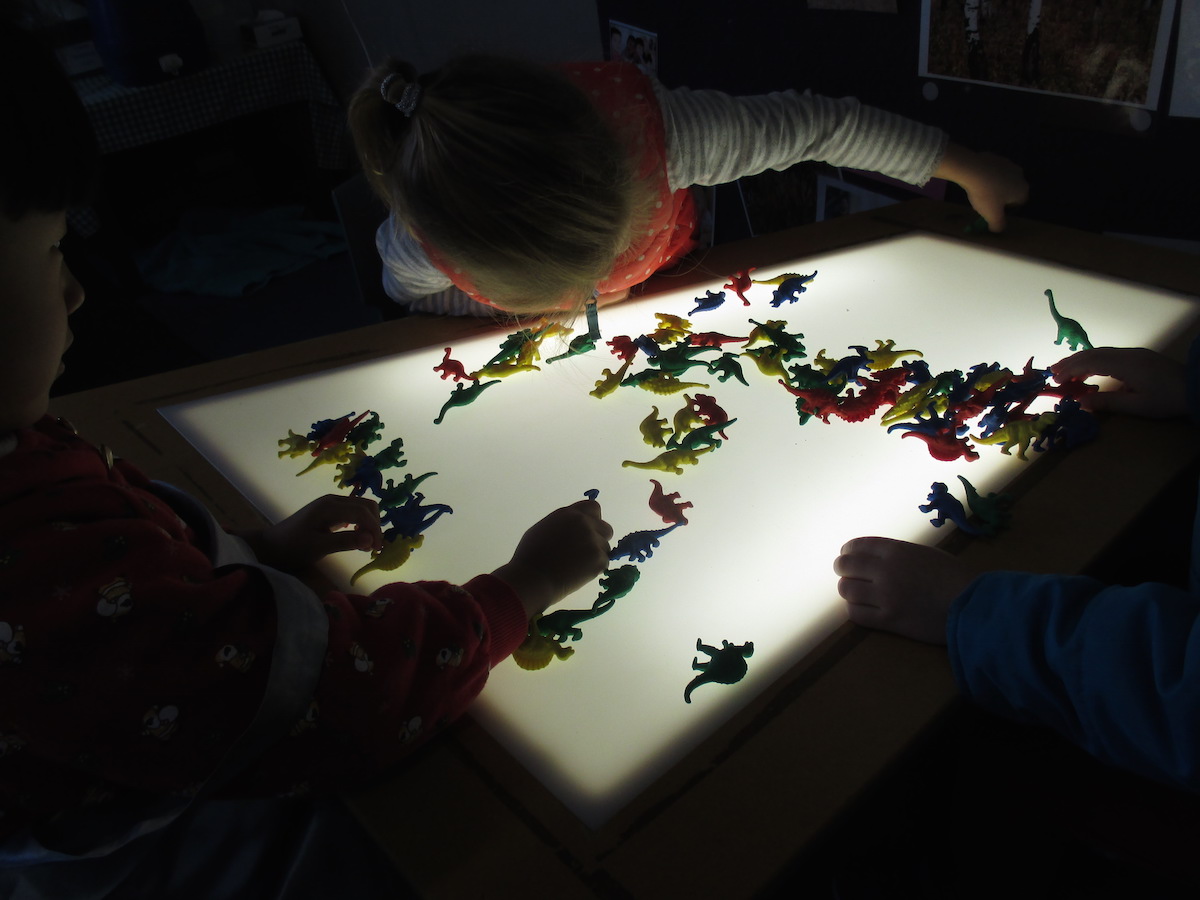 Kindy kids playing with dinosaur toys on a lightbox