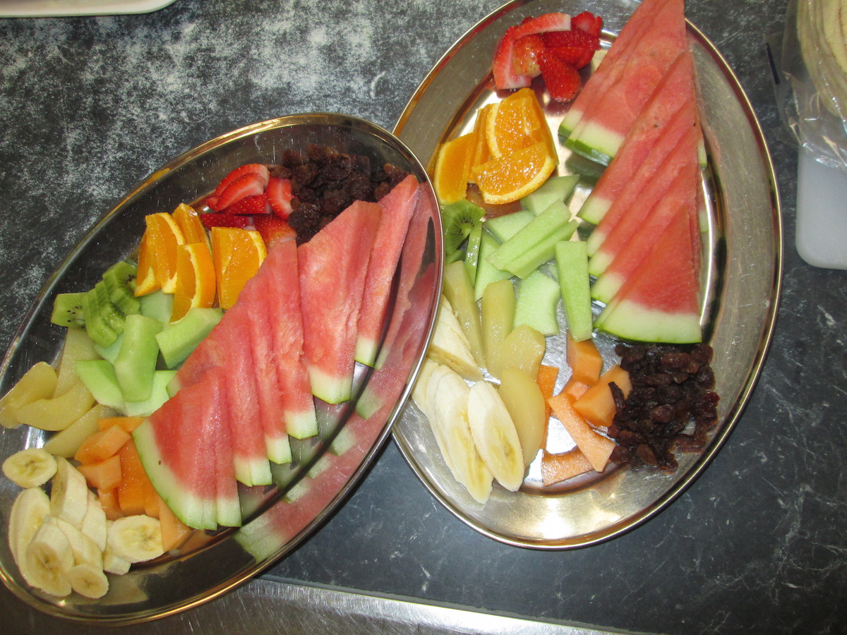 Morning fruit platter with banana, various melons, kiwifruit, strawberries, sultanas, oranges and apple.