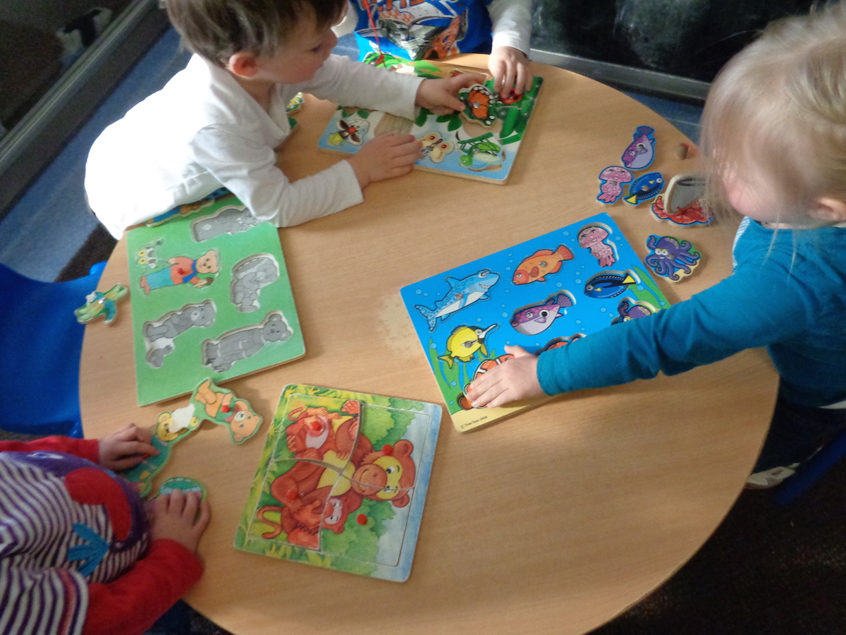 Toddlers playing with four wooden puzzles
