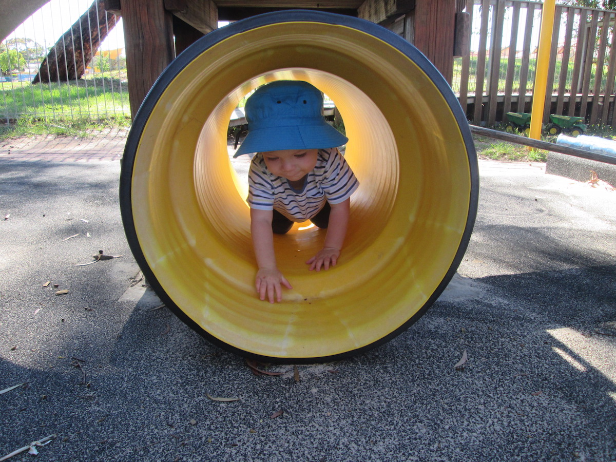 Young child crawling through a pipe in the babies play yard