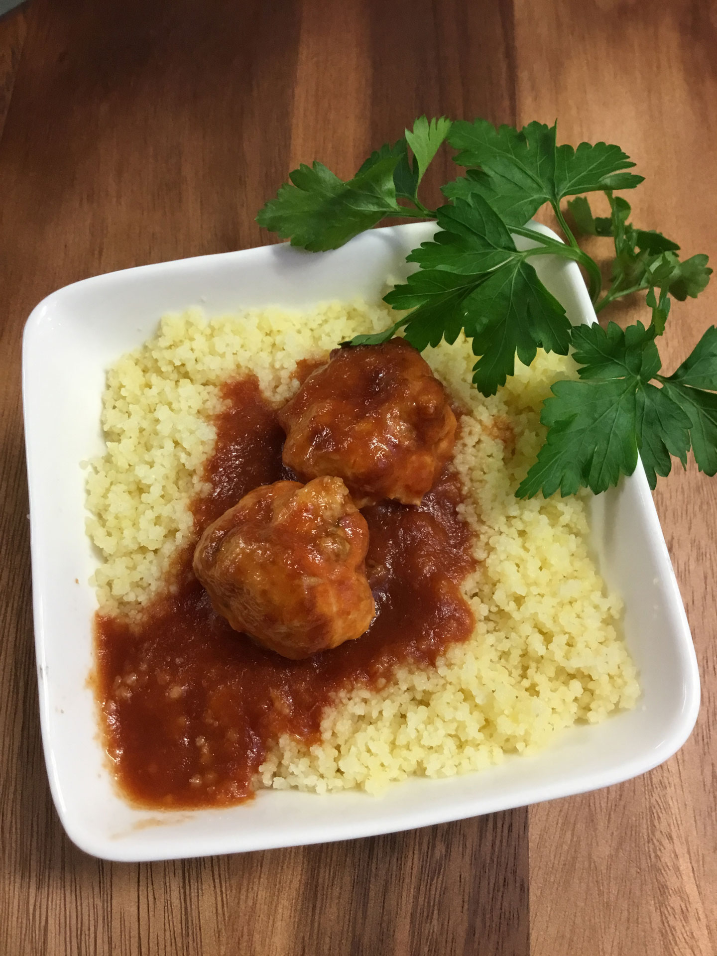 Cous cous and meatballs with marinara sauce, garnished with parsley