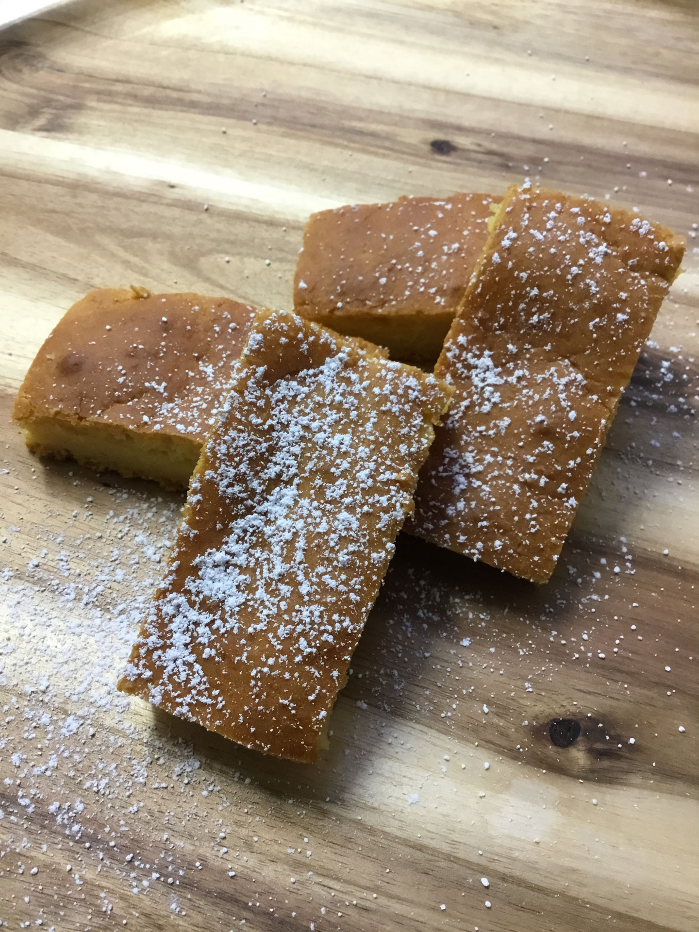 Four pieces of slice, dusted with icing sugar and arranged neatly on a board